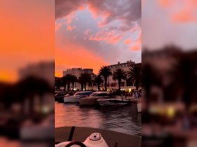 A stunning sunset casts vibrant colors over a bustling harbor filled with boats and palm trees, creating a picturesque scene perfect for evening strolls and waterfront dining.