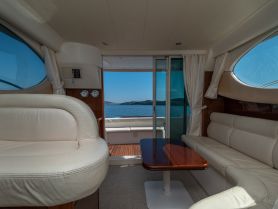 Interior view of a luxurious boat cabin featuring comfortable seating and a helm, with stunning views of the water through large windows.