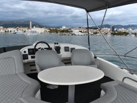 A well-appointed interior view of a boat's helm and seating area, showcasing comfortable furnishings and a scenic backdrop of the waterfront.