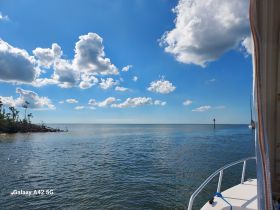 A serene view from the deck of a boat, showcasing calm waters and a clear blue sky with fluffy clouds — perfect for a relaxing day on the water.