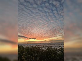 A stunning sunset over a beach with scattered clouds, featuring silhouettes of people enjoying the view. The vibrant colors create a picturesque scene perfect for evening strolls.