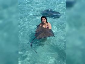 A woman joyfully interacts with a stingray in shallow turquoise waters, showcasing a memorable wildlife experience in a tropical paradise.