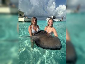 Two women interact with a stingray in the crystal-clear waters, showcasing a unique wildlife experience in a tropical paradise.