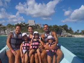 A joyful family poses together on a boat with the stunning Tulum ruins in the background, capturing a memorable vacation moment on the water.