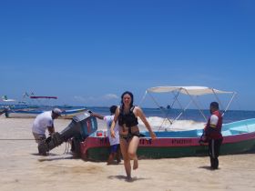 A woman joyfully runs from the water towards a boat, while crew members assist with the motor — capturing the excitement of a beach adventure.
