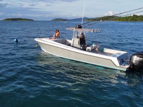 A woman relaxes on the bow of a fishing boat, surrounded by serene waters and distant islands, perfect for a day of adventure on the sea.