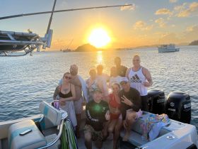 A lively group enjoys a sunset celebration aboard a boat, capturing the perfect moment with friends against a stunning backdrop of the setting sun.