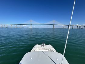 A stunning view of a boat's bow with a modern bridge in the background, showcasing the serene waters and clear blue skies — perfect for a day out on the water.