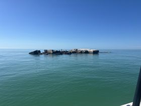 A distant view of a rocky formation in calm waters under a clear blue sky, lacking clarity and detail.