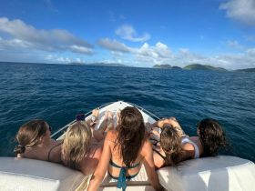 A group of friends relaxes on the bow of a boat, enjoying the stunning ocean views and nearby islands — a perfect moment for camaraderie and adventure on the water.