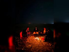 A group of friends gathers around a campfire at night, enjoying each other's company in a cozy outdoor setting — perfect for memorable adventures under the stars.