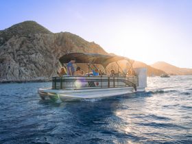 A lively group enjoys a scenic boat tour in Cabo, surrounded by stunning coastal views and the warm glow of sunset.