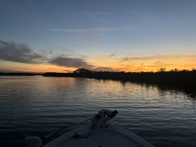 A serene sunset view from the bow of a boat, reflecting on calm waters, perfect for peaceful evening cruises.