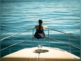 A woman enjoys a moment of tranquility at the bow of a boat, gazing out over calm waters — a perfect snapshot of relaxation on the open sea.