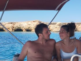 A couple enjoys a moment together on a boat, surrounded by stunning blue waters and rocky cliffs — perfect for romantic getaways or summer adventures.