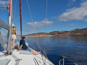 A couple enjoys a serene sailing experience on calm waters, with stunning mountain scenery in the background — perfect for a relaxing day on the boat.