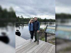 A cheerful couple poses on the dock by the lake, surrounded by serene nature — perfect for romantic getaways or outdoor adventures.