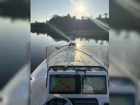 A view of the helm and navigation console on a boat, showcasing advanced charting technology and a serene waterway under the morning sun.