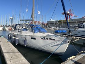 A beautiful view of the 'Indigo Blue' yacht docked at the marina, showcasing its sleek design and vibrant blue accents against a clear sky.