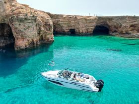 A stunning view of a boat anchored near rocky cliffs, with swimmers enjoying the crystal-clear waters — a perfect spot for exploration and adventure.