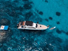A vibrant scene featuring a group enjoying a sunny day on a yacht, with paddleboarding and lounging on a floating mat in crystal-clear waters — perfect for summer adventures.