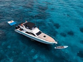 Aerial view of a lively scene with guests enjoying a floating mat and swimming near a stylish boat in crystal-clear turquoise waters — perfect for summer adventures.