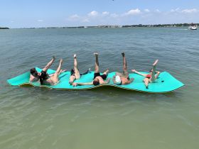 A lively group enjoys a sunny day on a floating mat in the water, showcasing the perfect summer fun and relaxation experience.