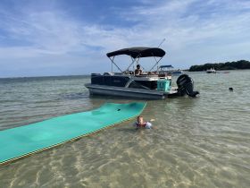 A child enjoys swimming near a pontoon boat, showcasing a fun day on the water with family-friendly activities.