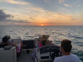 A group enjoys a stunning sunset aboard a pontoon boat, creating a perfect backdrop for memorable moments on the water.