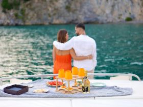 A couple enjoys a romantic moment on a boat, surrounded by delicious food and drinks, perfect for a sunset celebration on the water.