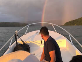 A stunning view of a rainbow over the water as a man enjoys the scenery from the boat — a perfect moment for nature lovers and adventure seekers.