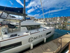 A sleek Lagoon catamaran named 'Mita' docked at a marina, showcasing its modern design against a backdrop of clear blue skies and calm waters.