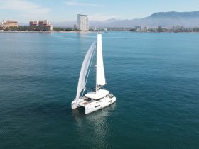 A stunning aerial view of a catamaran sailing through calm waters, showcasing its sleek design against a backdrop of coastal scenery.