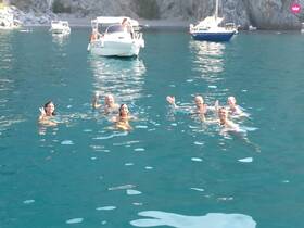 A cheerful group enjoys a refreshing swim in crystal-clear waters, with boats anchored nearby — perfect for a fun day on the water.