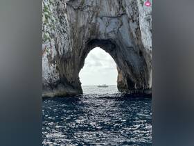 A stunning view of a boat passing through a natural rock arch, showcasing the beautiful ocean scenery — a perfect highlight of a coastal adventure.