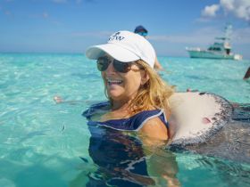 A woman joyfully interacts with a stingray while swimming in crystal-clear waters, showcasing a unique wildlife experience in a tropical paradise.