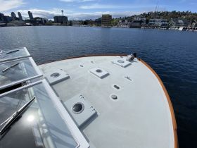 Aerial view of the front deck of a yacht, showcasing its sleek design against a backdrop of the city skyline and calm waters.