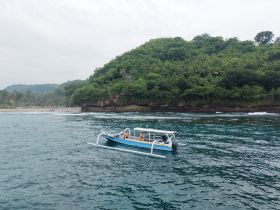 A traditional boat navigates the serene waters along a lush coastline, showcasing the beauty of the landscape and the joy of on-water exploration.