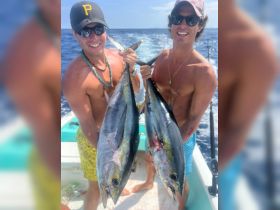 Two friends proudly display their impressive catch of fish while enjoying a day of fishing on the open ocean — a perfect moment of celebration and camaraderie.