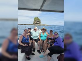 A cheerful group of friends enjoys a day on the water, posing together on a boat with a scenic rock formation in the background — perfect for memorable outings and celebrations.