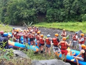 A large group gathers for a safety briefing before embarking on an exciting rafting adventure, surrounded by lush greenery and river scenery.