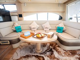 A cozy interior view of a yacht's lounge area featuring plush seating, decorative pillows, and a tray of refreshments, perfect for relaxing on the water.