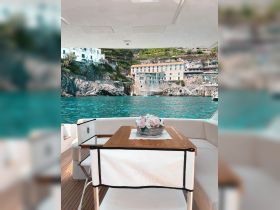 A beautifully arranged dining area on a yacht, featuring elegant seating and a floral centerpiece, perfect for enjoying meals while taking in stunning coastal views.