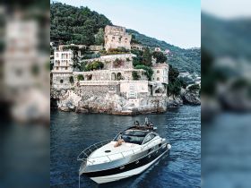 A woman relaxes on the deck of a luxurious boat, with stunning coastal architecture in the background — a perfect blend of relaxation and scenic beauty.