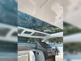 A sleek view of the helm inside a modern boat, showcasing the stylish interior and panoramic windows that offer stunning views of the surrounding cliffs.