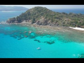 A stunning aerial view of a boat navigating through crystal-clear turquoise waters near a lush coastline, showcasing the beauty of the destination.
