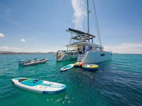 A luxurious catamaran anchored in clear waters, showcasing paddleboards and inflatable tubes ready for fun on the water. Perfect for adventurous outings and family activities.