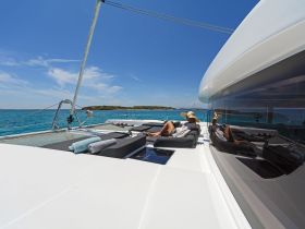 Two guests relax on the deck of a luxurious catamaran, enjoying the sun and stunning ocean views — an ideal setting for a tranquil getaway.