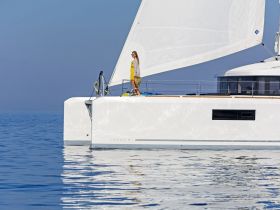A woman stands on the deck of a Lagoon yacht, enjoying a serene sailing experience on calm ocean waters — perfect for luxury getaways and sailing adventures.