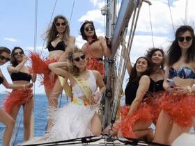 A lively group of friends celebrates aboard a sailboat, showcasing fun outfits and a festive atmosphere — perfect for bachelorette parties or summer outings on the water.